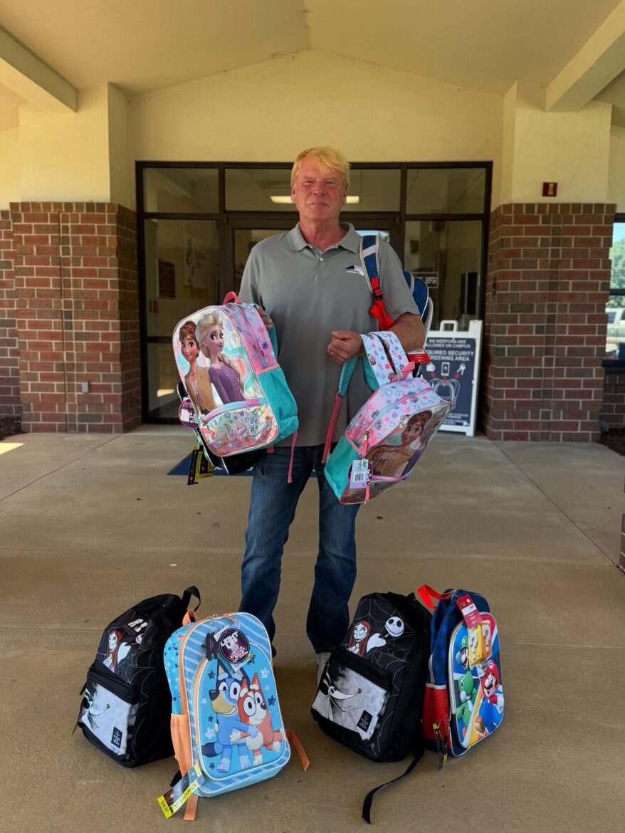 Neuse River Homes representative holding donated backpacks outside Glendale-Kenly Elementary School for the back-to-school supply drive