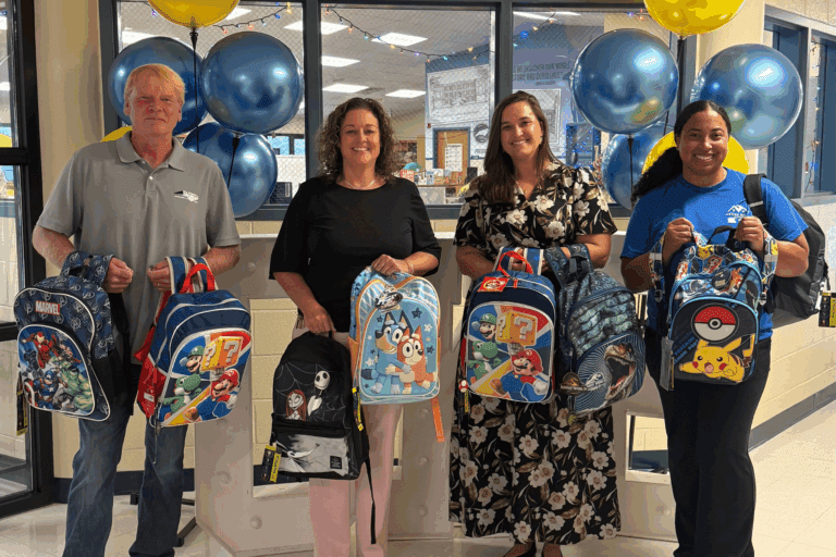 Neuse River Homes team members and school staff smiling with donated backpacks at Glendale-Kenly Elementary School.