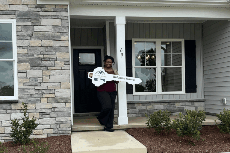 Happy homebuyer holding a Neuse River Homes key in front of her new Johnston County home, ready to move in